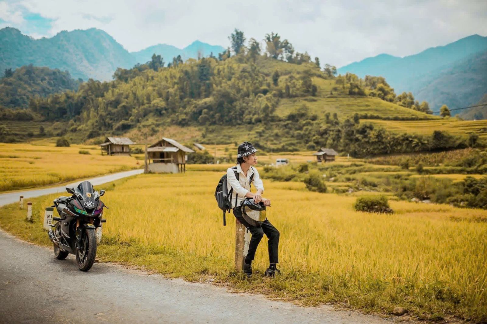 A traveller and motorbike beside golden fields on a village road