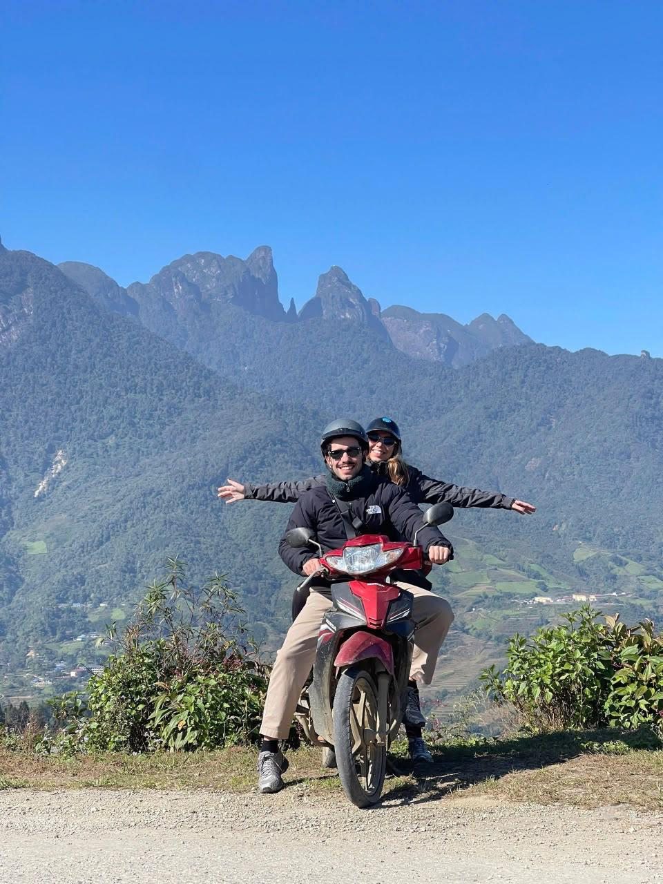 Guests posing on a motorbike with a mountain ridge behind them