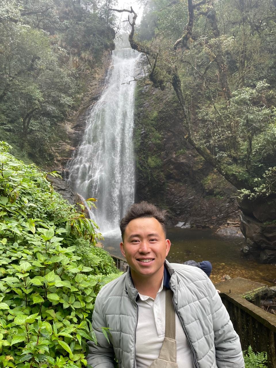 Chinh standing near a forest waterfall in Sa Pa